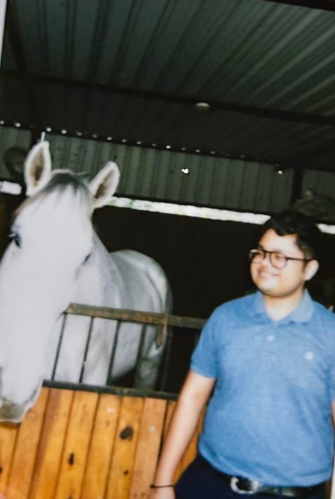 Instant photo of Tanuj smiling beside a white horse in a stable